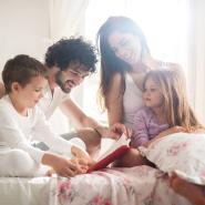 Mom and dad reading to their son and daughter on the bed. 